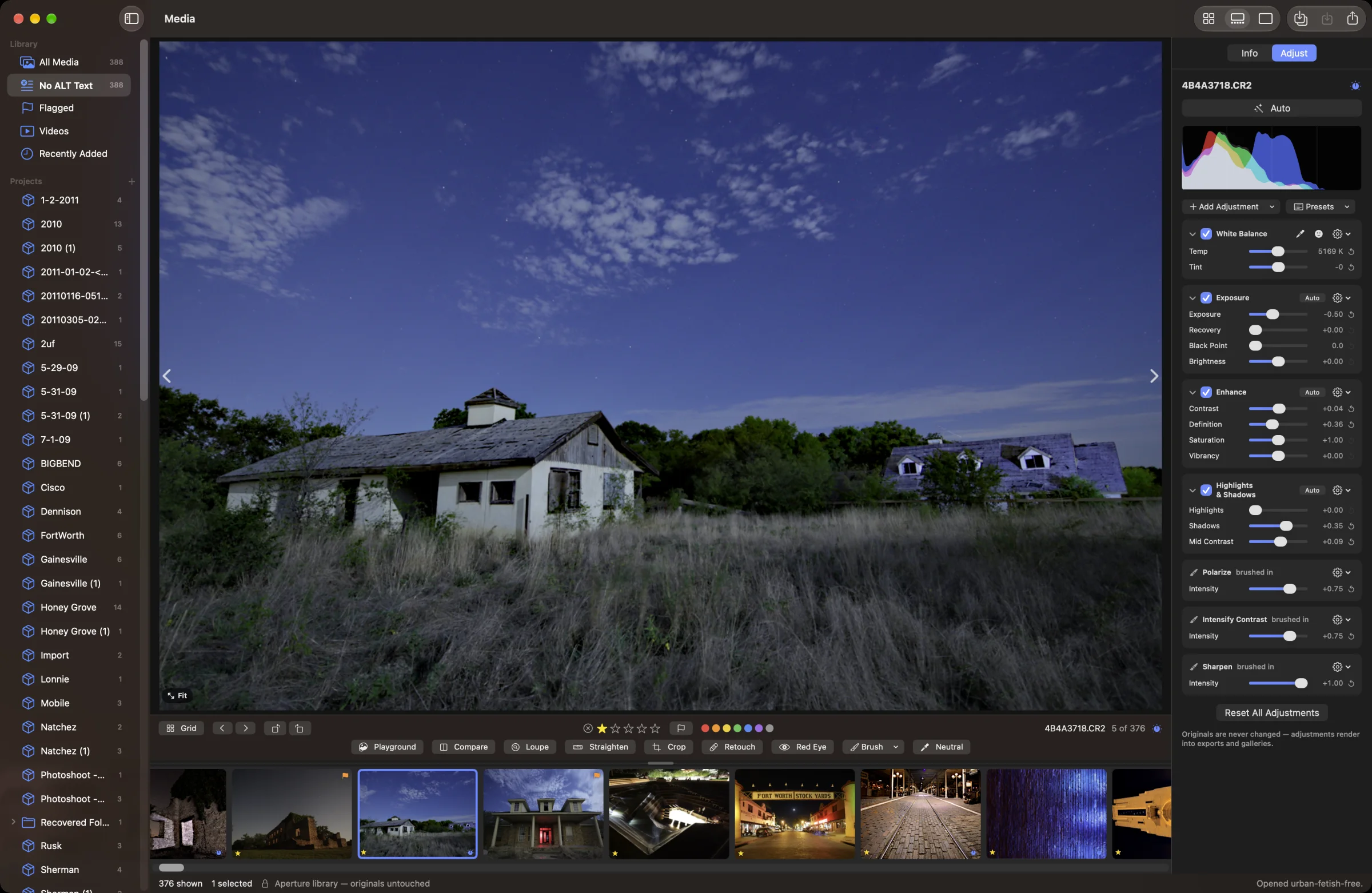 Alter in Split View: a moonlit abandoned farmhouse stands in tall grass under a deep blue night sky streaked with cloud, with a second house behind it and a filmstrip of night photos below. The Adjust inspector on the right shows a live RGB histogram above the photo’s bricks — White Balance at 5169 K, Exposure −0.50, Enhance with Definition +0.36, Highlights & Shadows with Shadows +0.35 — and three brushed-in bricks: Polarize, Intensify Contrast and Sharpen. A note at the bottom reads “Originals are never changed — adjustments render into exports and galleries.”