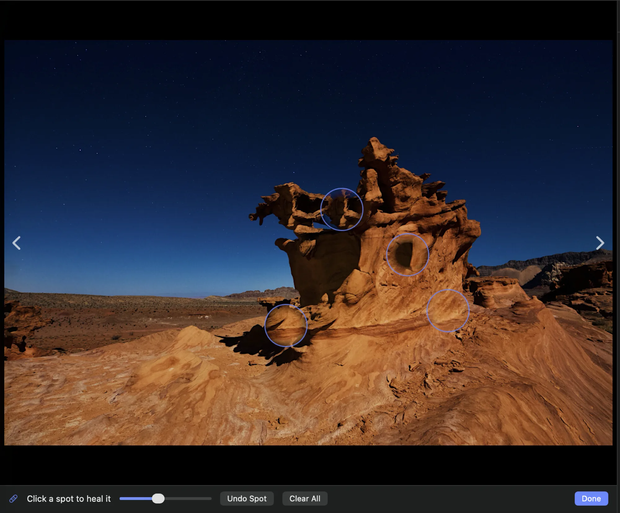 Retouch mode over the sandstone formation: four accent-colored ring markers sit on the rock where spots have been placed. The tray reads “Click a spot to heal it” beside a spot-size slider, with Undo Spot, Clear All, and Done.