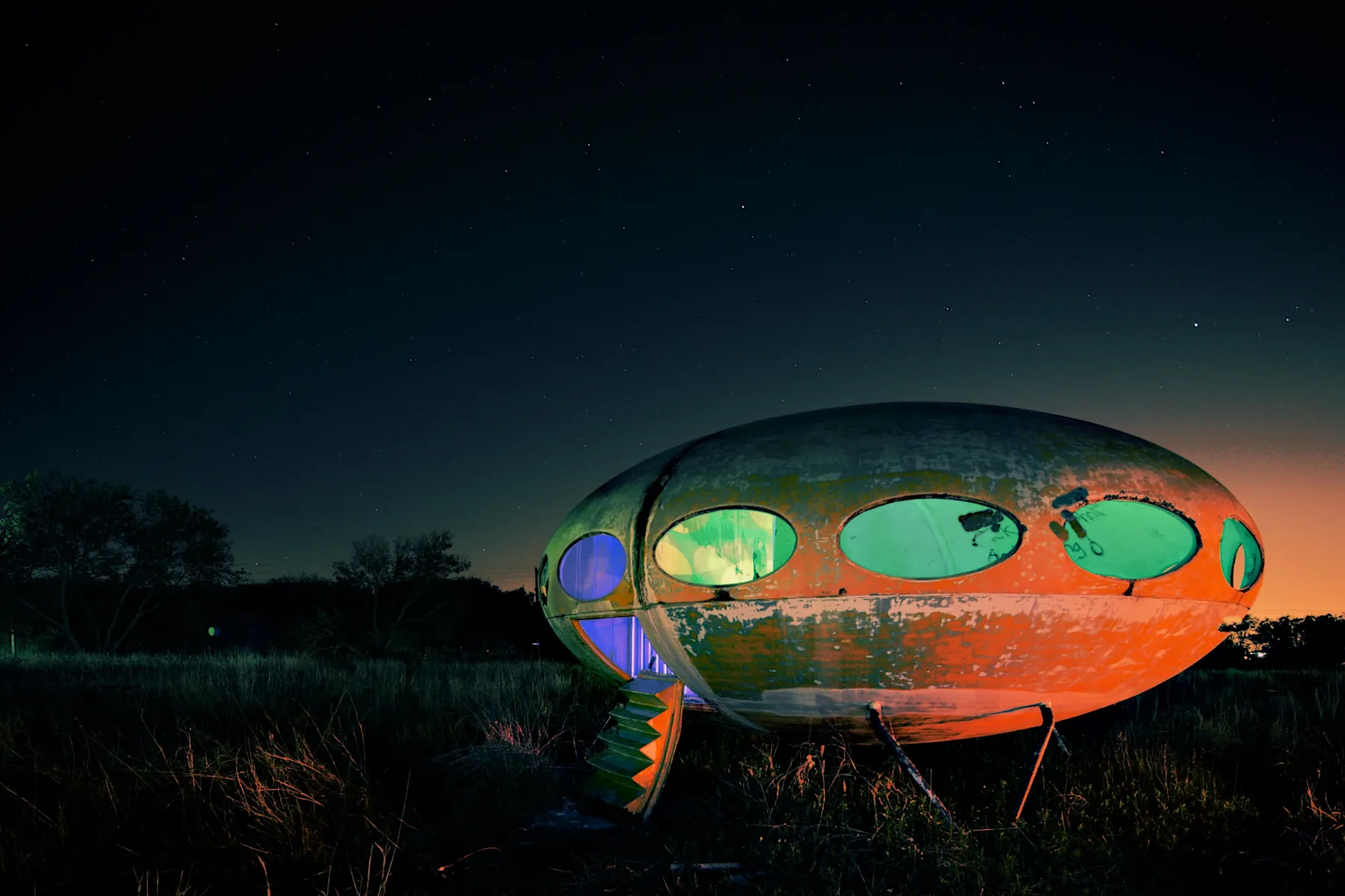 The Futuro house with its Aperture edit, rendered by Alter: a deep blue night sky, the saucer’s rusted shell glowing orange, its windows lit pale green and violet.